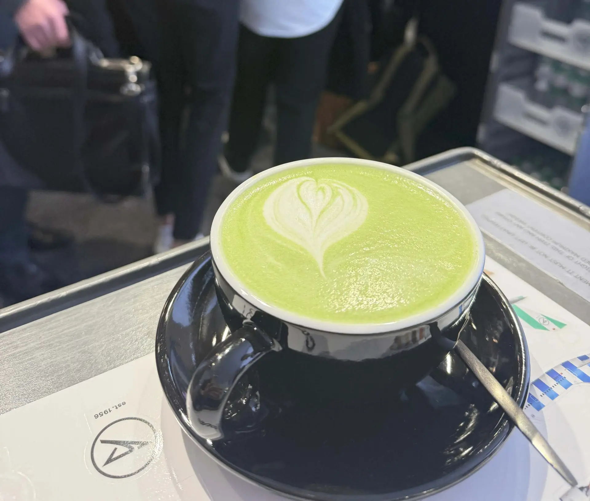 Matcha Latte Macchiato mit Latte Art in einer Tasse, serviert auf einem professionellen Kaffeecatering-Stand bei Messe oder Event.